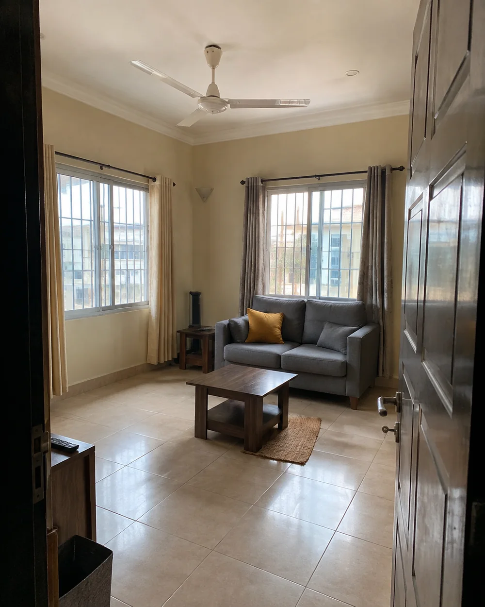 A Yaba-style living room with a grey sofa, tiled floor and broad windows